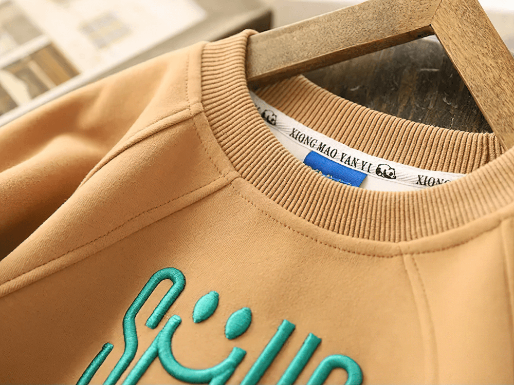 Soft beige kids sweatshirt with "SMILE" graphic in vibrant teal, featuring cozy fabric and trendy style.